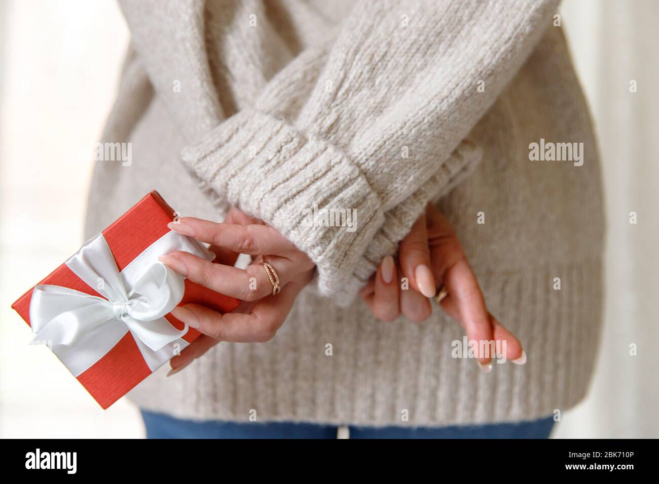 La femme veut donner une surprise cadeau dans une boîte rouge à son petit ami et inquiète, a traversé ses doigts, vue du dos. Banque D'Images
