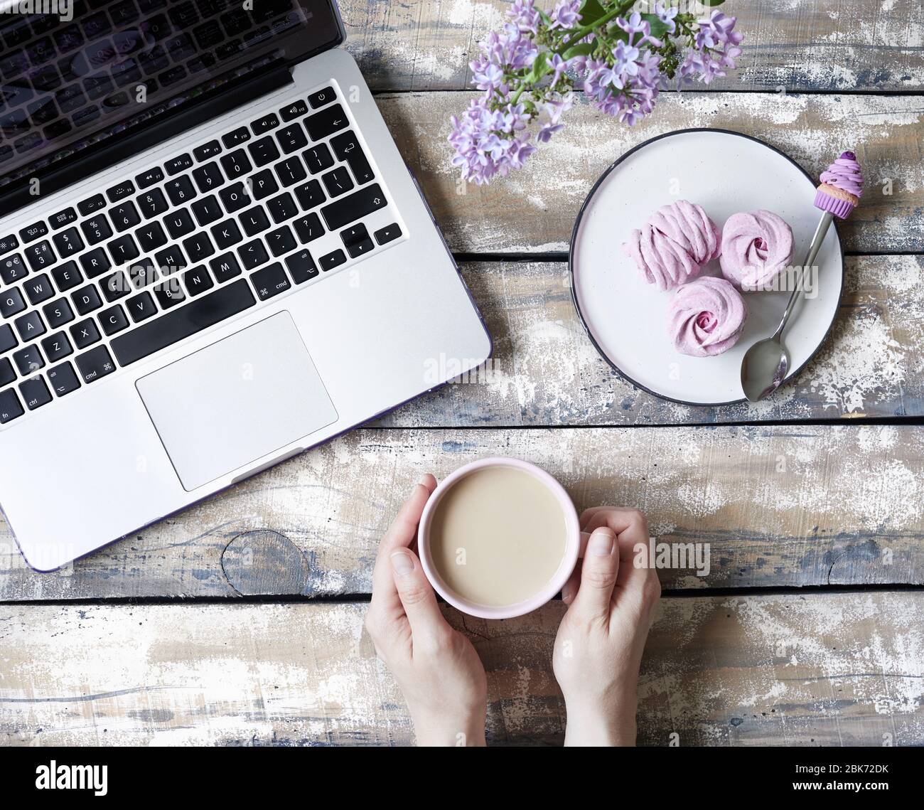 Femme travaillant à la maison, boire du café au lait et manger du Zephyr ou Marshmallow doux maison violet de cassis près de l'ordinateur portable et du bouquet lilas Banque D'Images