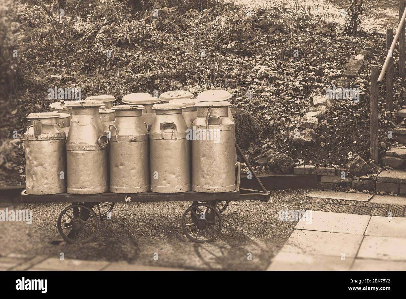 Sepia, churns de lait d'époque en trolley à la gare du patrimoine, Severn Valley Railway, Royaume-Uni. Production et distribution de lait britannique. Lait Royaume-Uni. Banque D'Images
