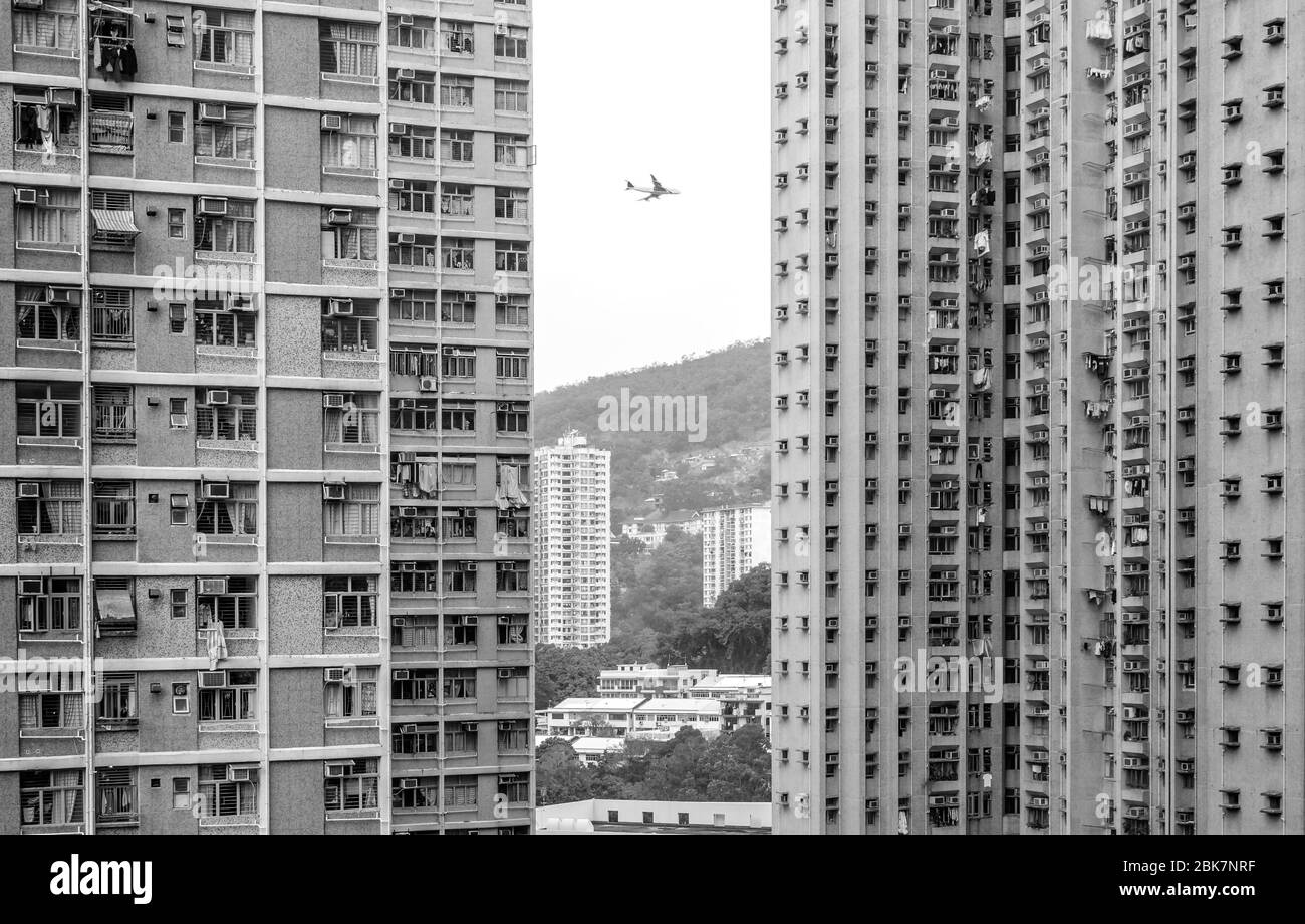 Vue en noir et blanc de l'avion volant entre les bâtiments résidentiels de haute hauteur, Hong Kong Banque D'Images