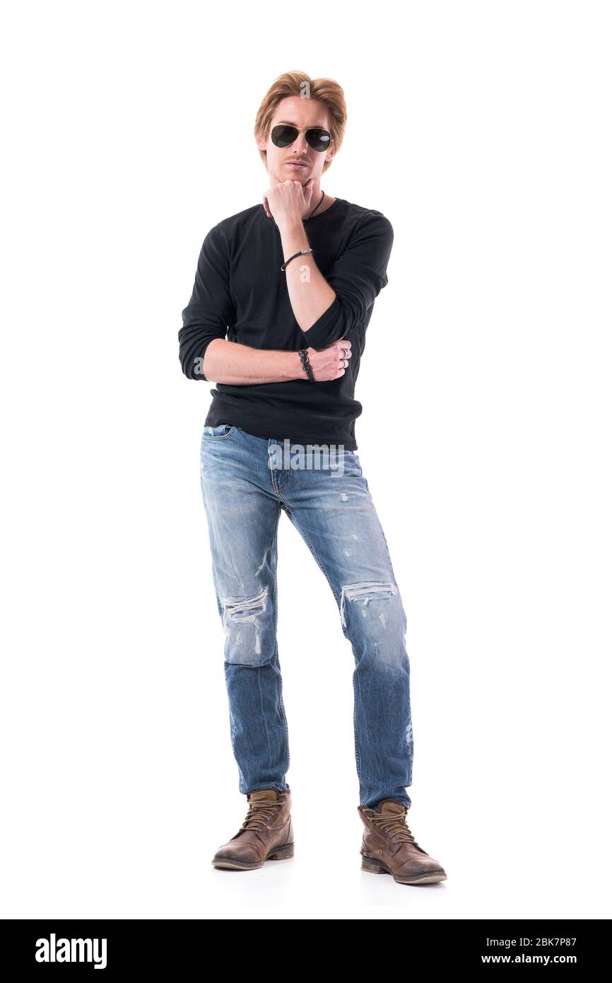 Mécontent jeune homme sérieux avec lunettes de soleil choisissant et analysant avec la main sur le menton. Corps entier isolé sur fond blanc. Banque D'Images