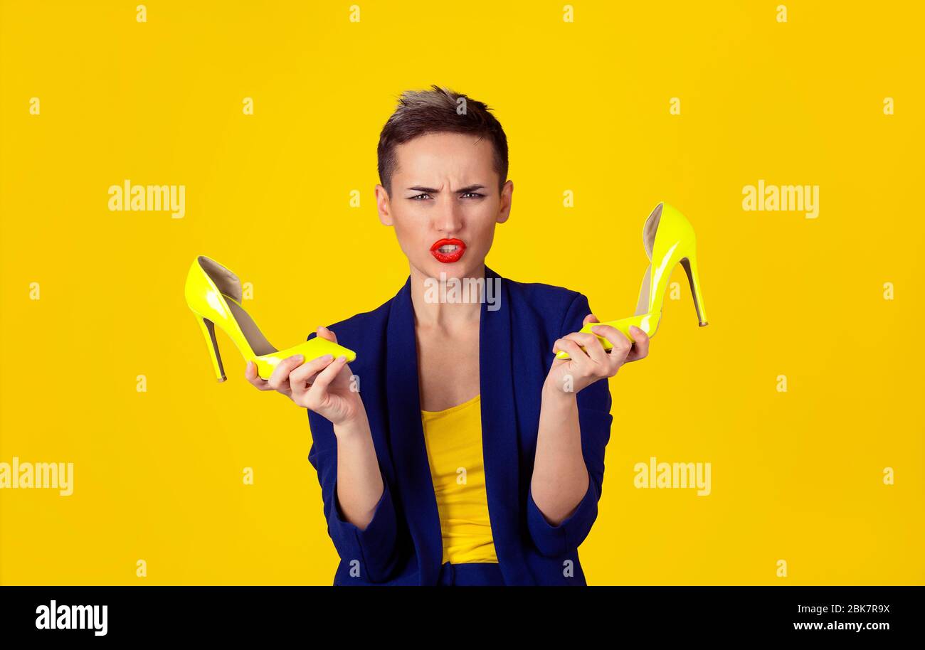 Jolie jeune fille millénaire tenant une paire de talons hauts modernes et élégants, profondément mécontente de les porter isolés sur blanc. Je n'aime pas hi Banque D'Images