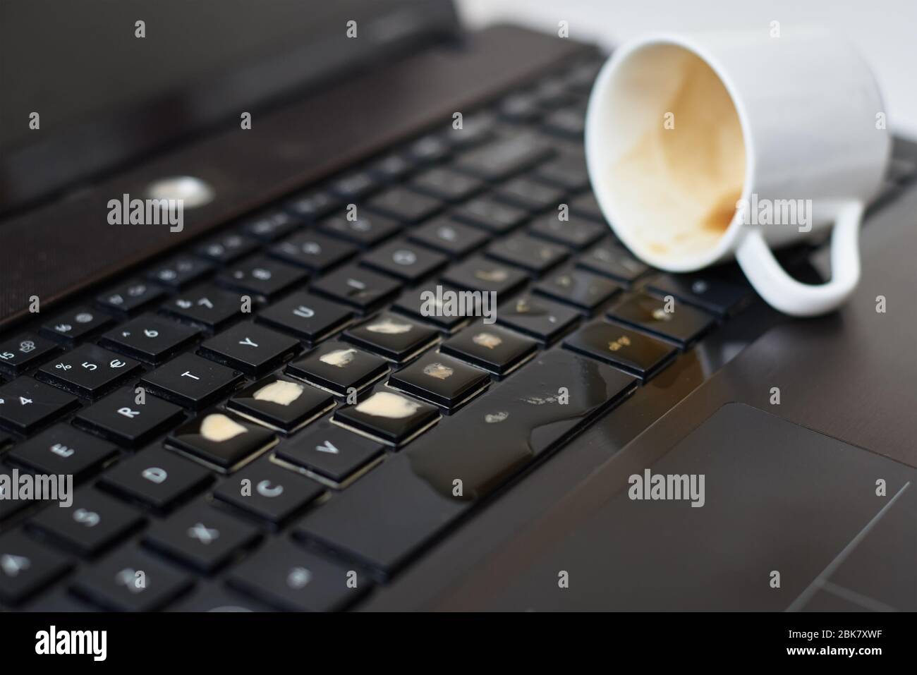 Renversez du café dans la tasse blanche sur le clavier de l'ordinateur portable. L'ordinateur est endommagé en raison d'un liquide renversé Banque D'Images Renversez du café dans la tasse blanche sur le clavier de l'ordinateur portable. L'ordinateur est endommagé en raison d'un liquide renversé Banque D'Images