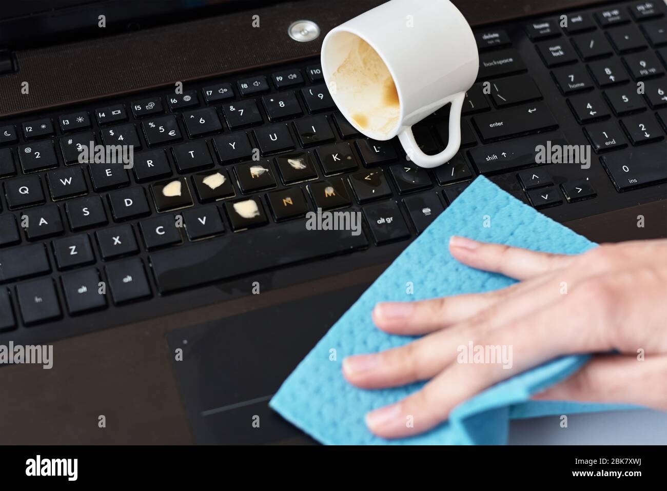 La main nettoie le café renversé sur le clavier de l'ordinateur portable avec un chiffon Banque D'Images La main nettoie le café renversé sur le clavier de l'ordinateur portable avec un chiffon Banque D'Images