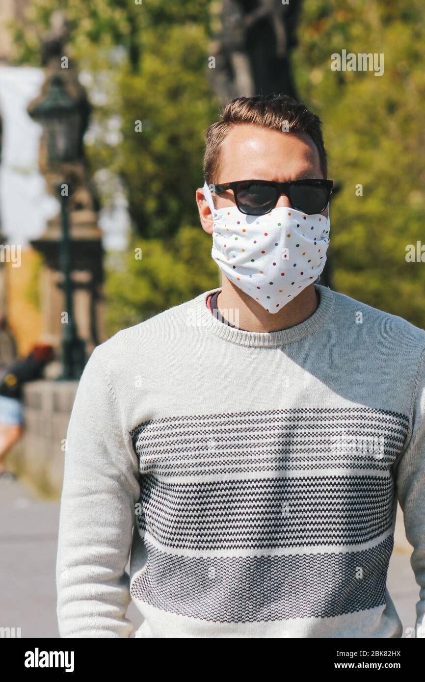Jeune homme avec lunettes de soleil et masque en tissu cousu photographié sur le pont Charles à Prague, en République tchèque. Arrière-plan flou. Voyager, tourisme pendant coronavirus. COVID-19. Photo verticale. Banque D'Images