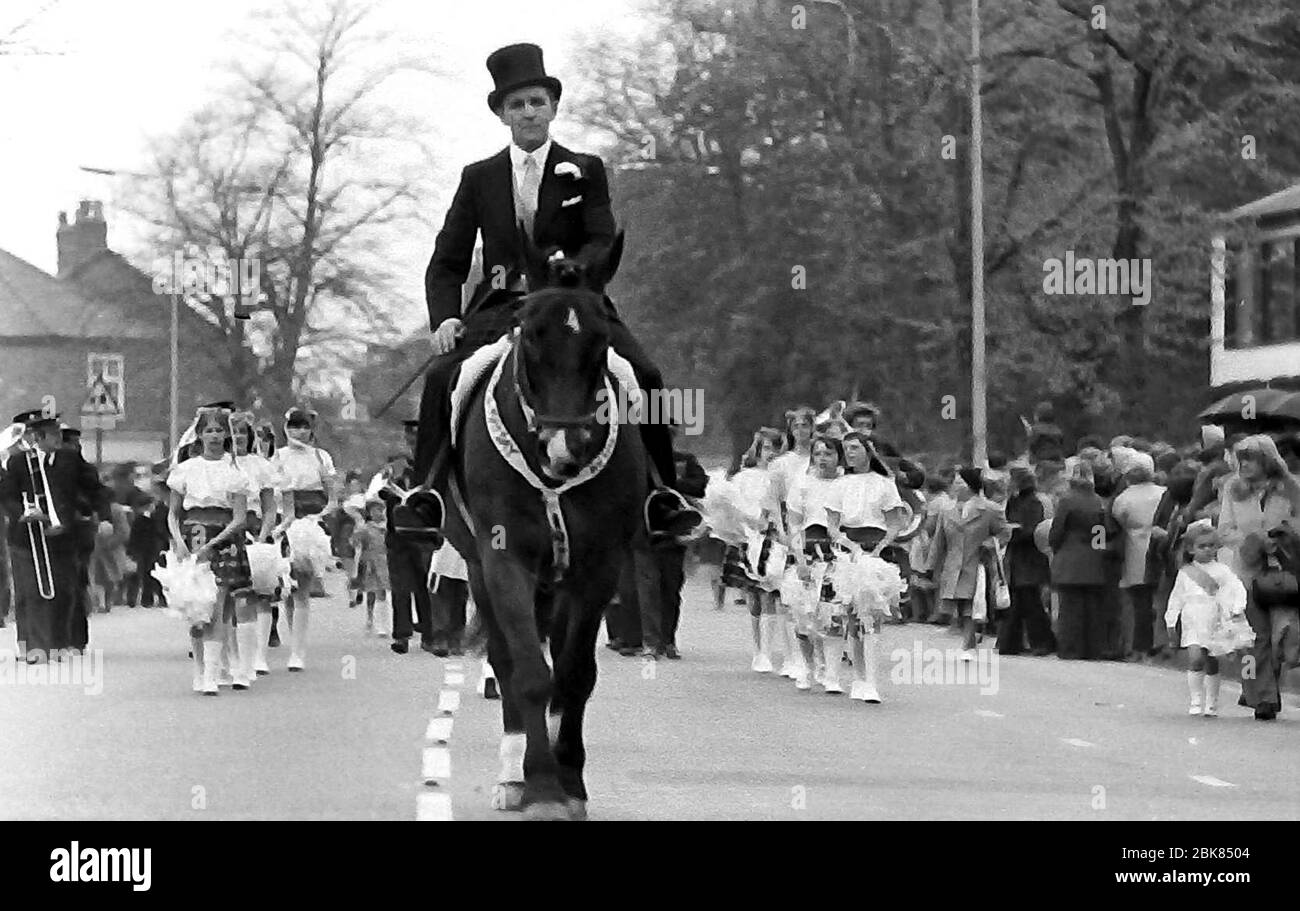 La procession annuelle de la Knusford Royal May Day en 1976 à Knusford, Cheshire, Angleterre, Royaume-Uni. Il comprend traditionnellement un spectacle de déguisements fantaisie d'enfants dans des costumes historiques ou légendaires avec des calèches. Un homme portant un chapeau de tête fait un cheval dans la procession, suivi d'un groupe de jeunes filles en costumes. Banque D'Images