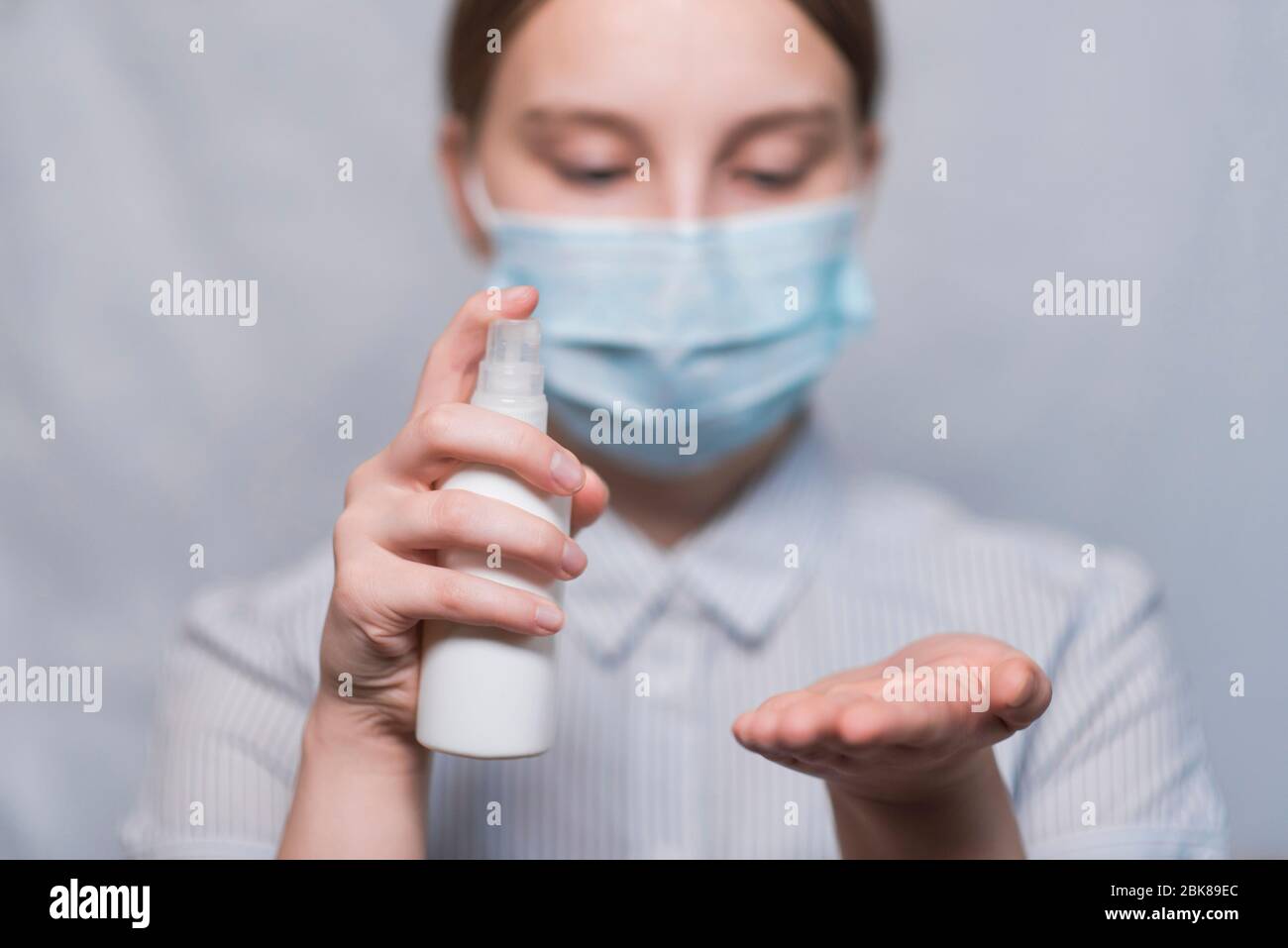 Une jeune fille de 12-15 ans, masque médical couvre le visage, contient un spray antiseptique à la main, désinfecte les mains des bactéries de virus, épidémie COVID-19 Banque D'Images