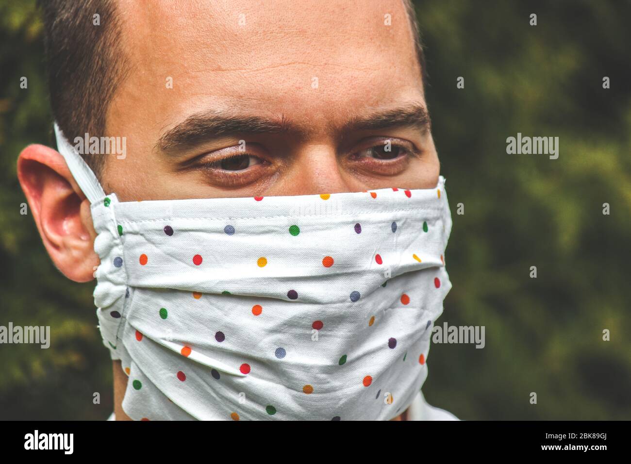 Jeune homme caucasien avec un masque de visage fait main en tissu pendant la pandémie de coronavirus. Coronavirus, éclosion de COVID-19. Concept de protection antivirus. Arrière-plan flou. Détail visage et yeux. Banque D'Images