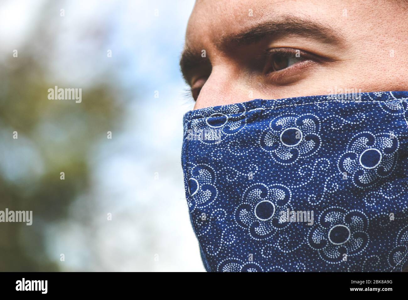 Jeune homme blanc barbu avec un masque de visage en tissu bleu pendant la pandémie de coronavirus. Coronavirus, éclosion de COVID-19. Concept de protection antivirus. Arrière-plan flou. SRAS-COV-2. Banque D'Images