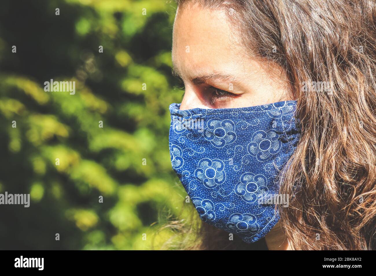 Jeune femme caucasienne à l'extérieur avec un masque de visage en tissu bleu pendant la pandémie de coronavirus. Coronavirus, éclosion de COVID-19. Concept de protection antivirus. Arrière-plan flou. SRAS-COV-2. Banque D'Images