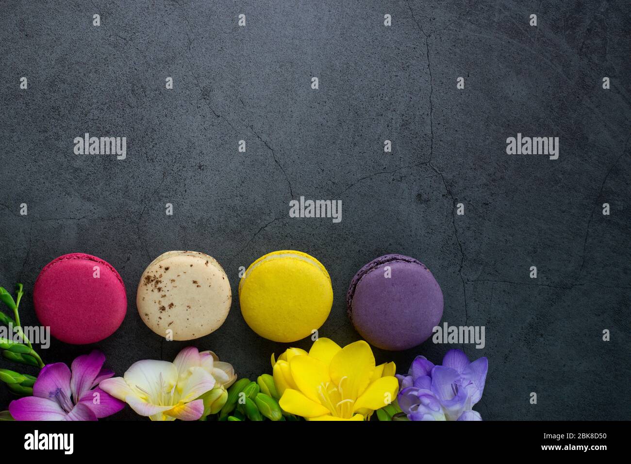 Carte de vœux colorée concept.bouquet de fleurs Freesia et macarons colorés sur fond de pierre grunge noire. Affiche pour les femmes jour, mariage Banque D'Images