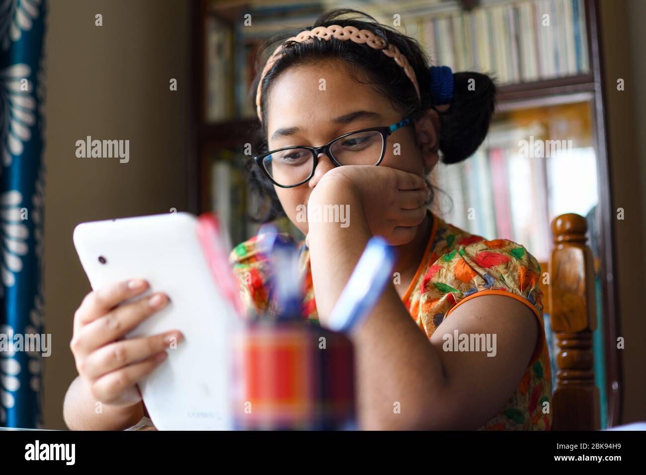 Adorable fille indienne qui étudie à la maison avec une tablette mobile dans la main Banque D'Images