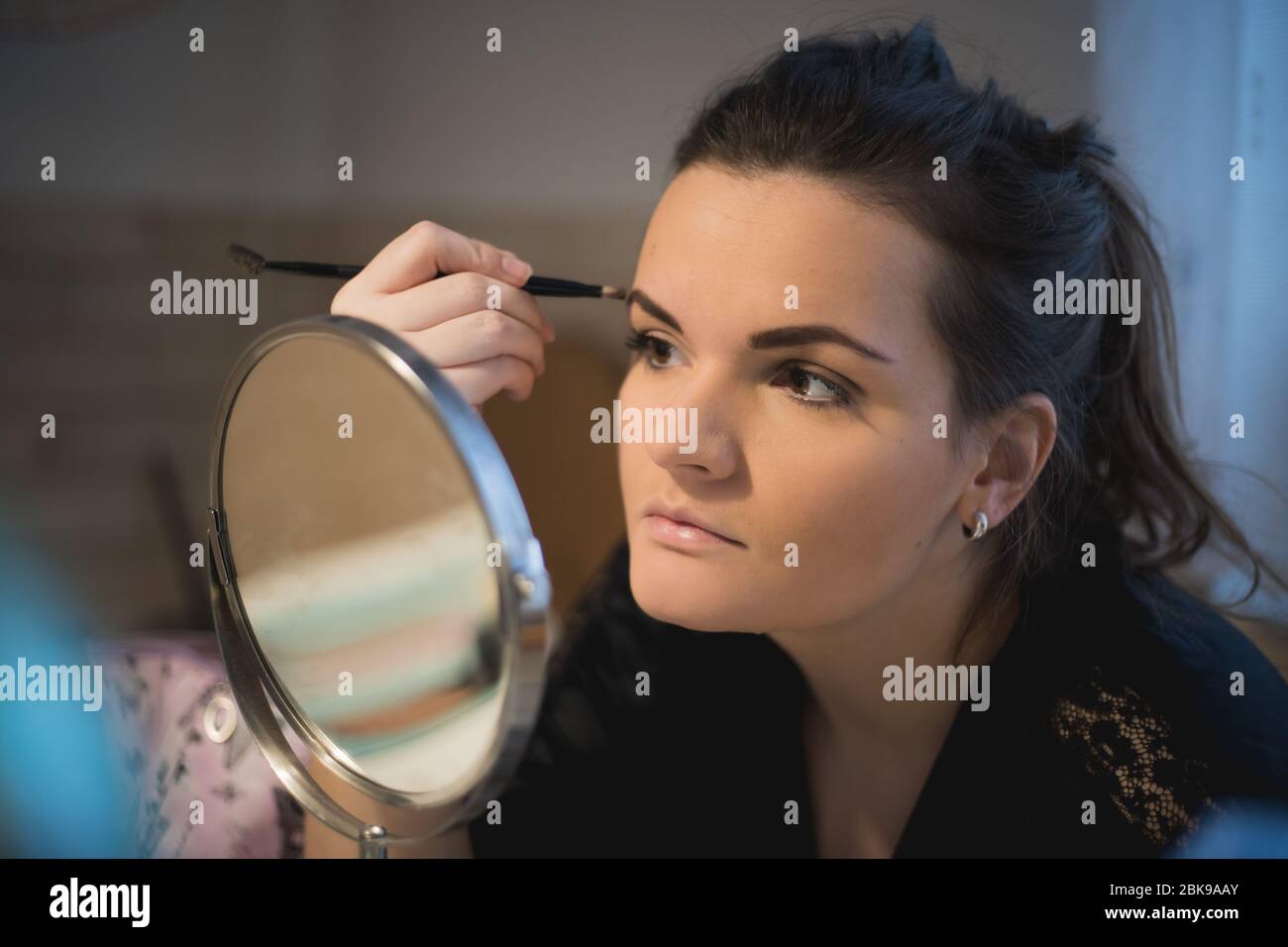 Portrait de la jeune femme regardant le miroir et le toilettage elle-même et tenant une brosse pour sourcils. Concept de maquillage. Banque D'Images