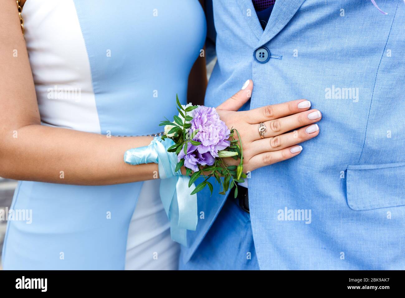 Jeune femme avec une boutonnière fleurie sur la main dans une robe bleue  embrassant un homme dans un costume bleu Photo Stock - Alamy