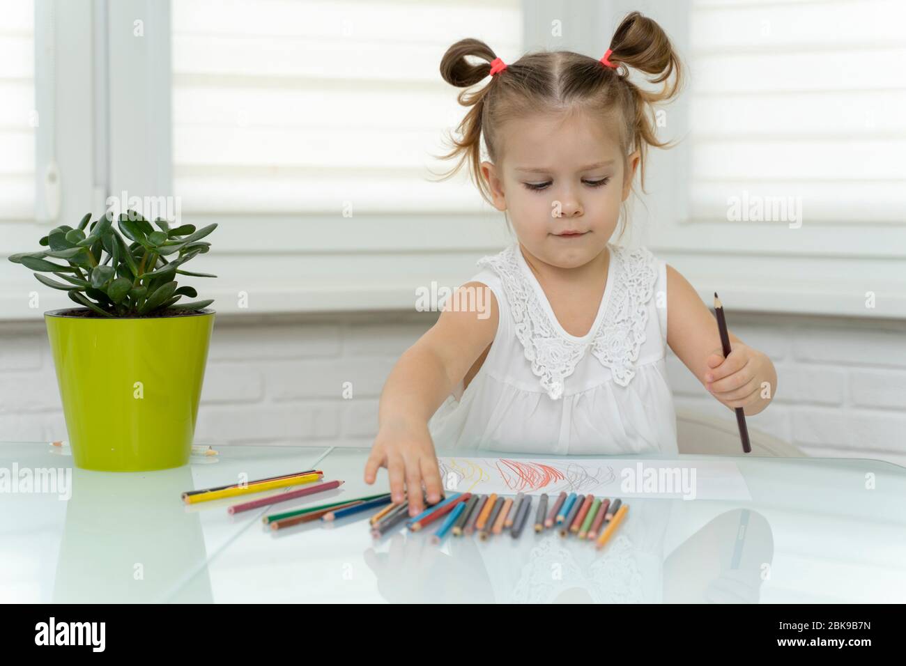 La petite fille de 4 ans dans un masque jetable attire des crayons à la maison à la table. La créativité des enfants sur l'auto-isolation à la maison Banque D'Images