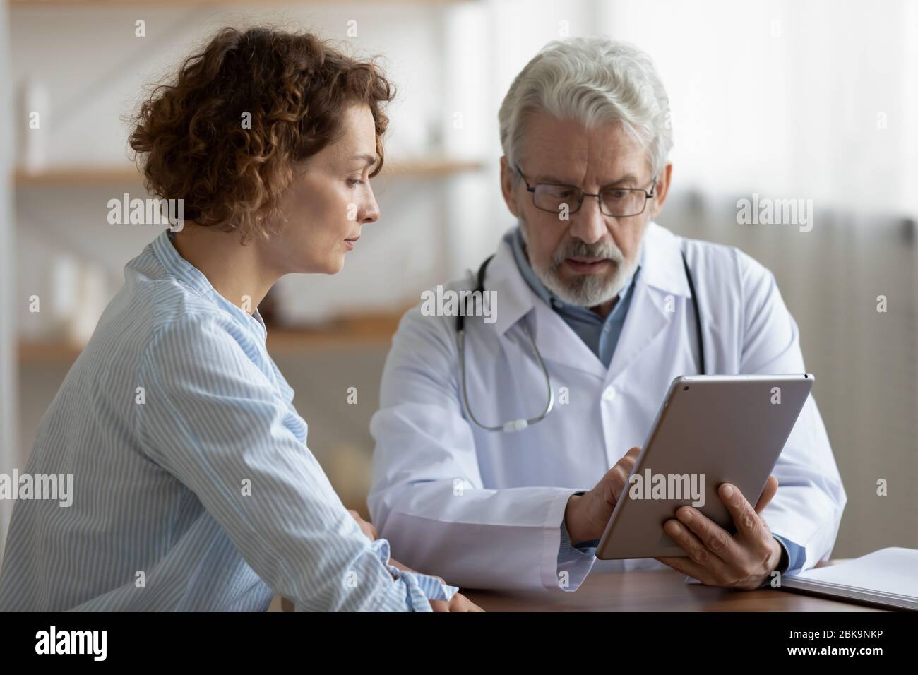 Médecin plus âgé consultant une jeune femme patient en utilisant une tablette numérique Banque D'Images