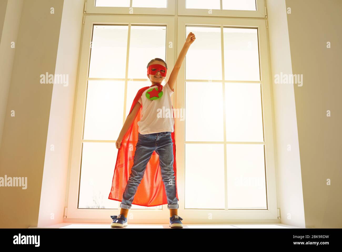 Enfant super héros.Kid sourire jouant un super héros s'amuser dans une chambre avec une fenêtre. Banque D'Images