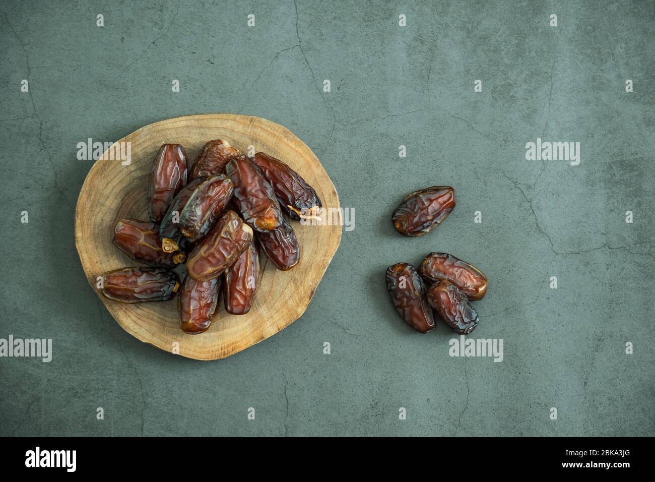 Fruits de date crus prêts à manger dans un plateau en bois sur fond de béton. Une cuisine traditionnelle, délicieuse et saine pour le ramadan. Flat lay, vue de dessus. Banque D'Images