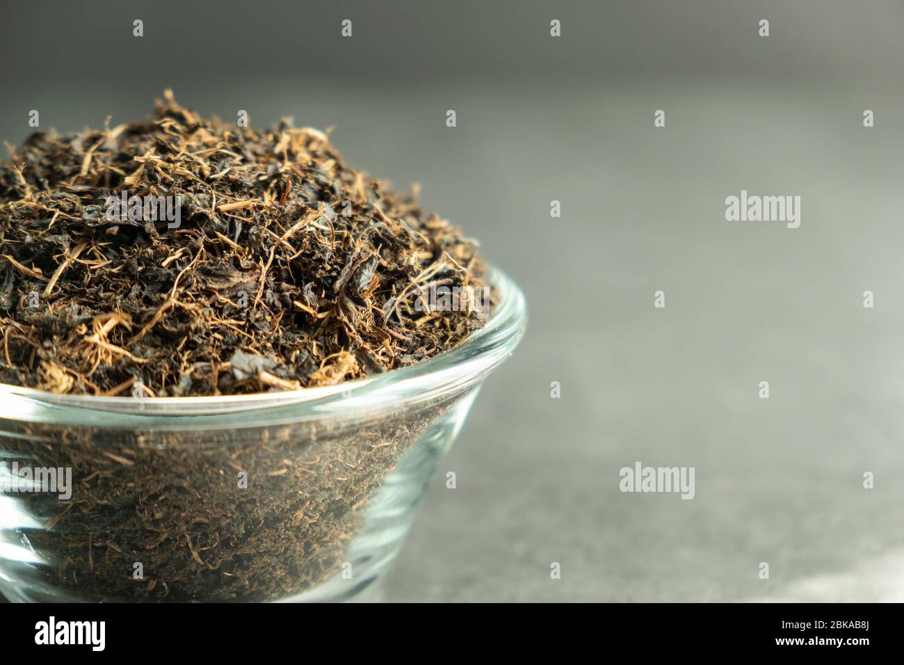 Sécher la feuille de thé noire dans un bol en verre sur fond de béton, en pierre. Boisson traditionnelle, saine et biologique. Banque D'Images