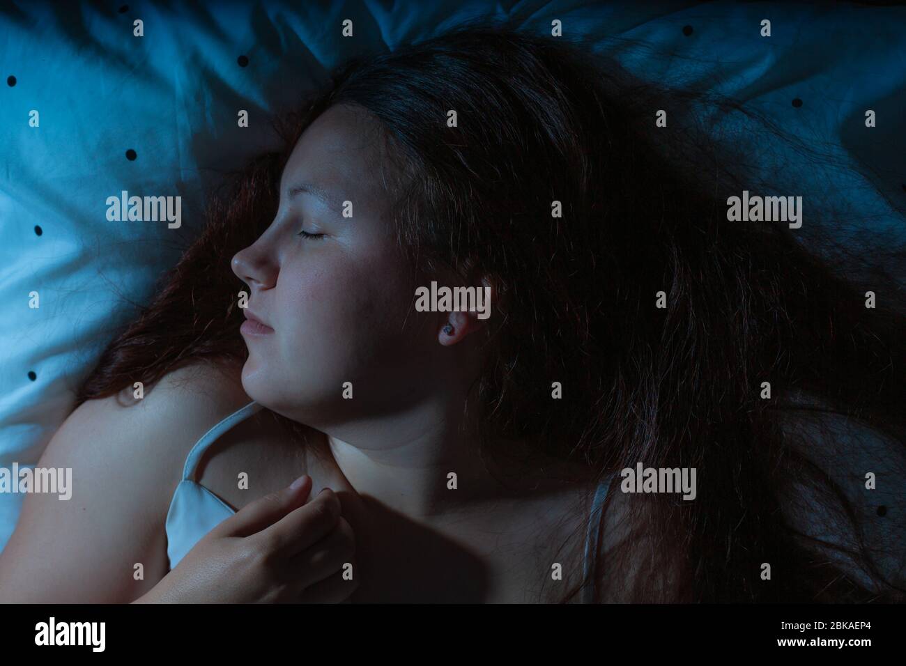Vue de dessus de la jeune femme dormant dans un lit la nuit, bleu nuit couleurs Banque D'Images