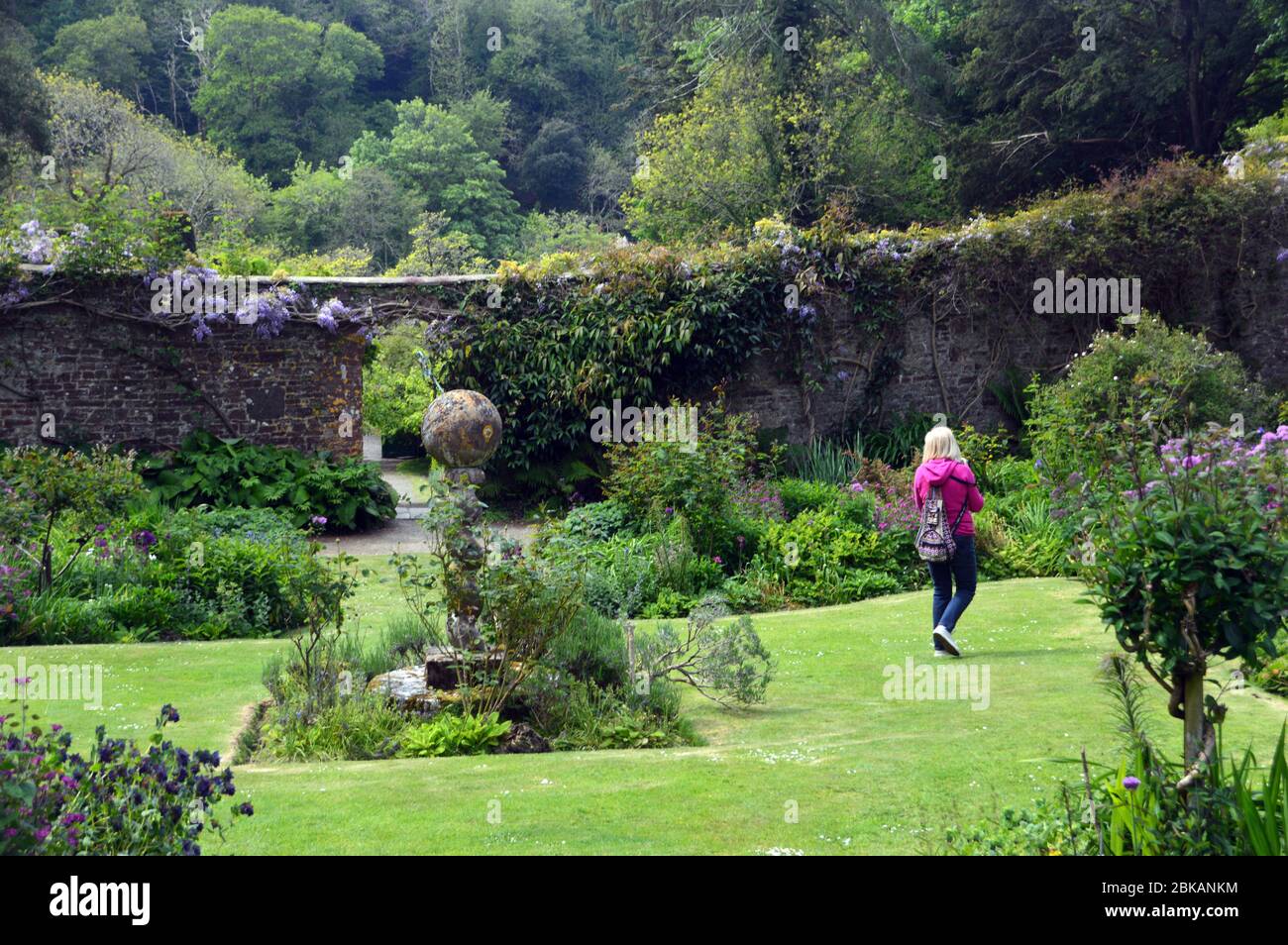 Femme marchant par une pierre Sculpture d'un cadran solaire dans le jardin clos à l'abbaye de Hartland Estate and Gardens, North Devon. Angleterre, Royaume-Uni. Banque D'Images