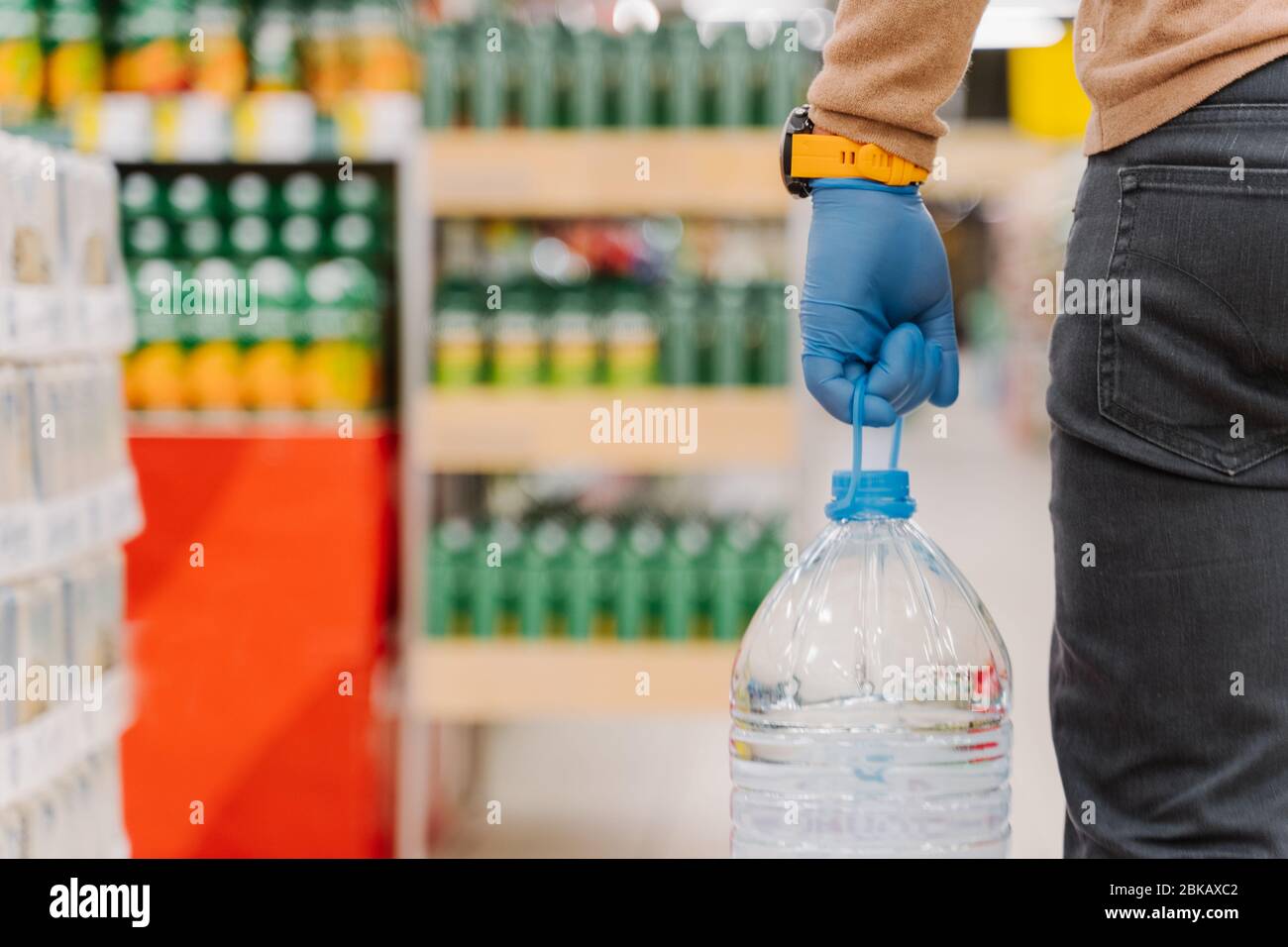 Panique shopping pendant la pandémie de coronavirus. Homme méconnaissable shopper porte des gants en caoutchouc, porte une bouteille d'eau potable, pose dans le supermarché, nous Banque D'Images