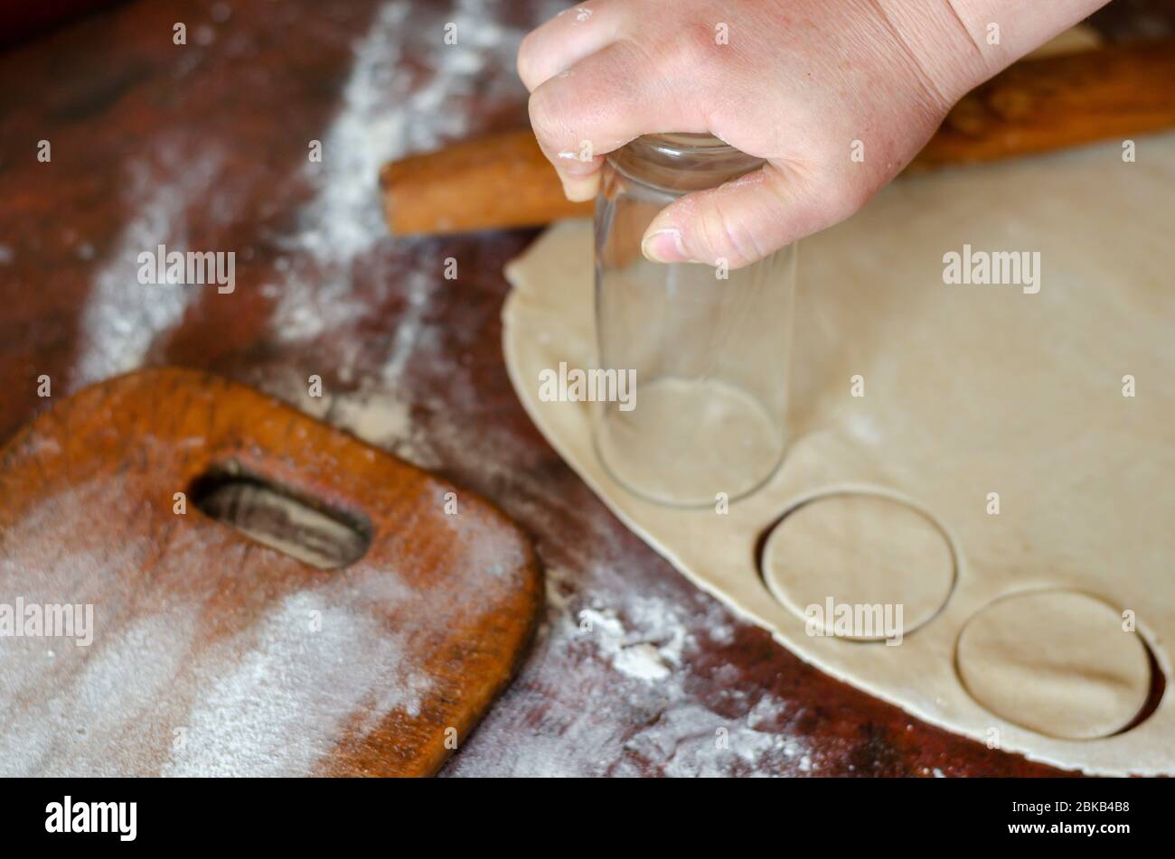 Une main féminine découpe des cercles dans une feuille de pâte avec un verre.  Pâte à pâte fine roulée pour boulettes de viande sur la table de cuisine.  Le processus de cuisson