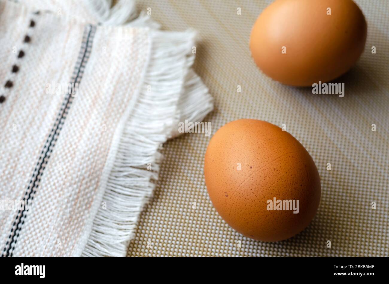 Deux œufs de poulet brun et une serviette de cuisine. Gros plan d'œufs de ferme non cuits sur beige. Une serviette pliée et une paire d'œufs. Vue de dessus à un angle. Sélectif Banque D'Images