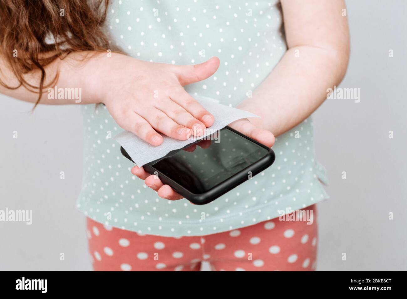L'enfant désinfecte l'écran du téléphone. Il est nettoyé en enlevant les microbes avec des lingettes humides antibactériennes pour éviter le coronavirus Banque D'Images