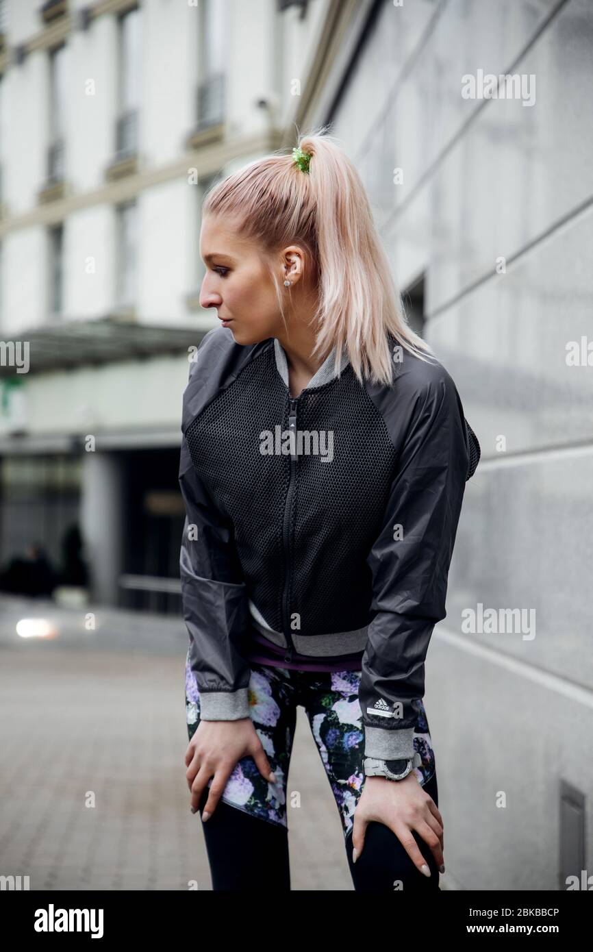 Jolie blonde fille avec queue de cheval est l'entraînement dans les vêtements de sport dans les rues d'une ville. Elle porte une veste, des leggings et des baskets sport. Banque D'Images