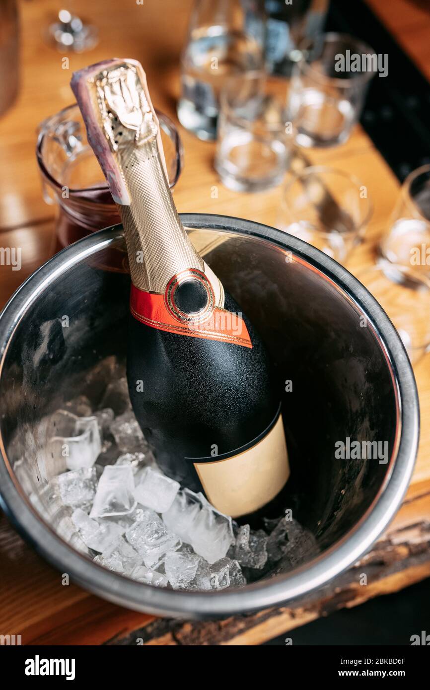 une bouteille de champagne dans un seau avec glace sur le fond d'une table en bois sur laquelle sont des verres Banque D'Images