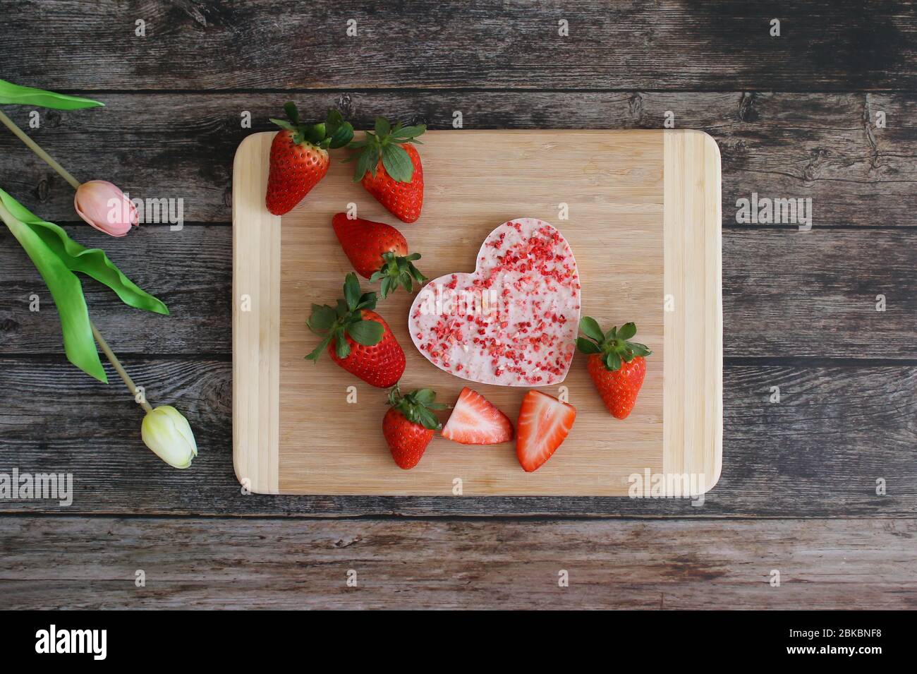 Chocolat aux fraises en forme de cœur sur une assiette en bois avec des fraises fraîches. Arrière-plan de table en bois avec fleurs de tulipe. Fond de carte de vœux. Banque D'Images