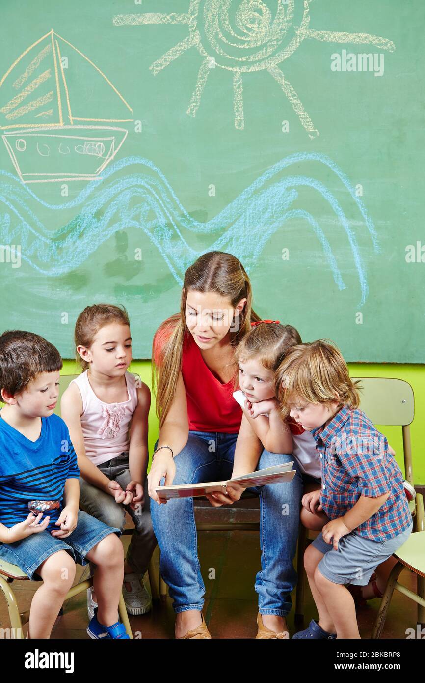 Les éducateurs et de nombreux enfants d'un groupe lisent un livre à la maternelle Banque D'Images