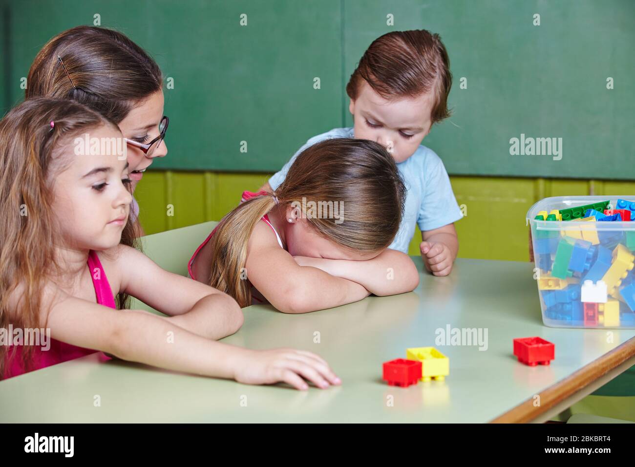 Un enfant triste pleut à la maternelle et est réconforté par le professeur de maternelle Banque D'Images