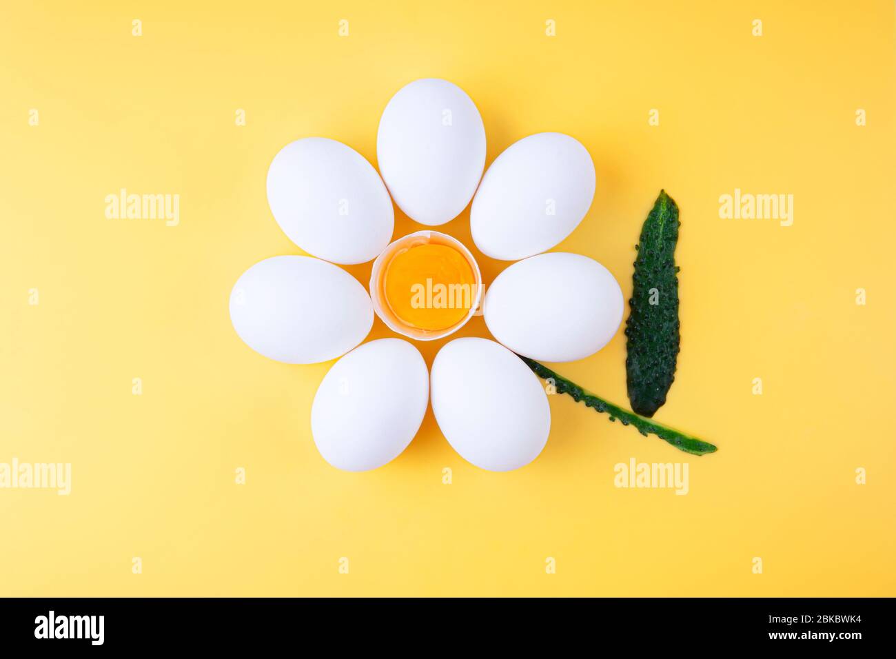 Oeufs de poulet disposés en forme de fleur avec jaune d'œuf exposé au milieu et pelure de concombre comme tige. Banque D'Images