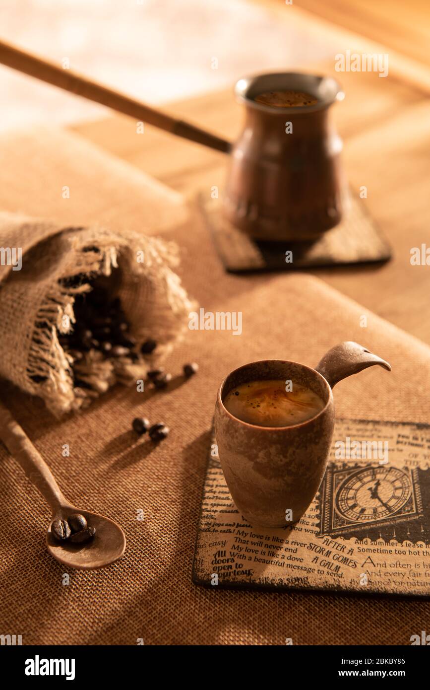 Petite tasse d'espresso glacé sur les montagnes russes avec du texte, sac de burlap non concentré avec des grains de café, cuillère avec des haricots et cafetière sur les genoux et sur la table. S Banque D'Images