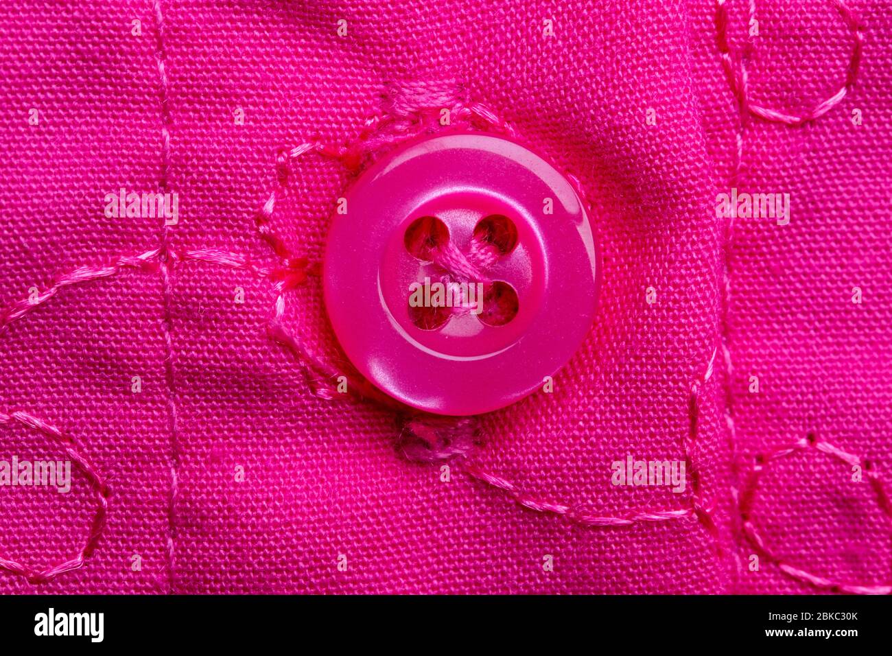 Macro photographie d'un bouton rose cousu sur un tissu rose avec broderie. Détail gros plan d'une petite robe pour filles. Banque D'Images