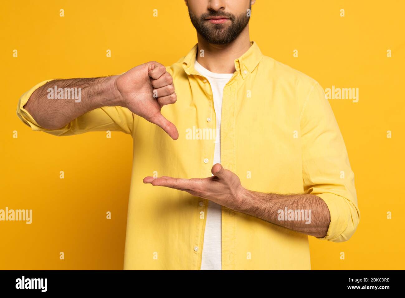 Vue réduite de l'homme barbu montrant le geste en langue sourde et sourde sur fond jaune Banque D'Images