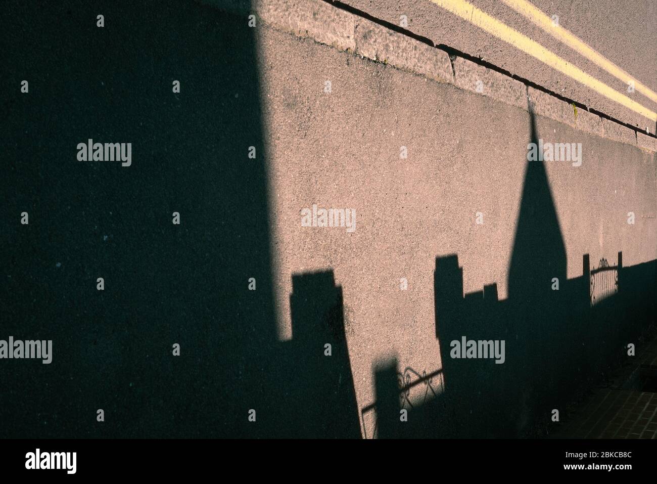 Ombres d'un toit pointu et portes avant sur un pavé ou un trottoir le long d'un trottoir et de lignes doubles jaunes Banque D'Images