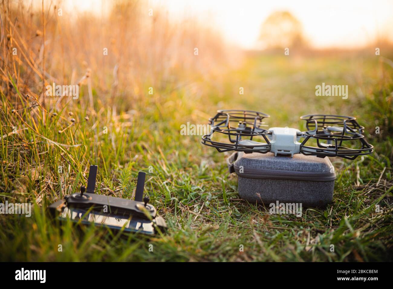 Petit drone avec protection de l'hélice sur boîtier gris avec téléphone de contrôle sur fond vert en été avec lumière chaude au coucher du soleil Banque D'Images