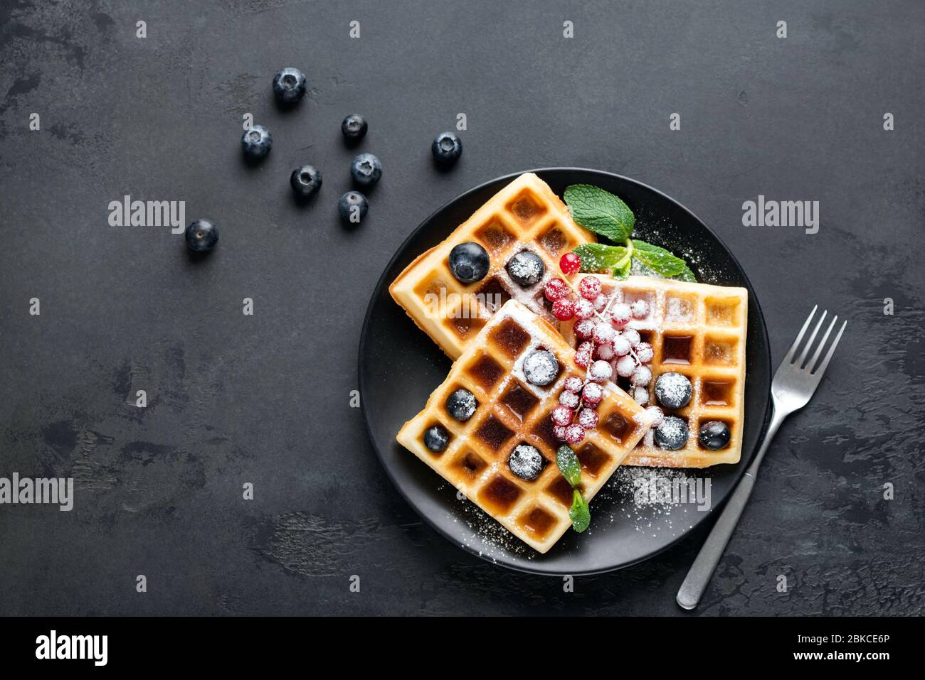 Gaufres belges carrées avec baies et sucre glace sur plaque noire, fond noir avec espace de copie. Table vue sur le dessert sucre sur la plaque Banque D'Images
