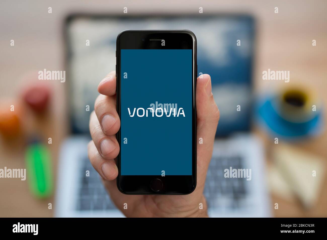 Un homme regarde son iPhone qui affiche le logo Vonovia (usage éditorial uniquement). Banque D'Images Un homme regarde son iPhone qui affiche le logo Vonovia (usage éditorial uniquement). Banque D'Images