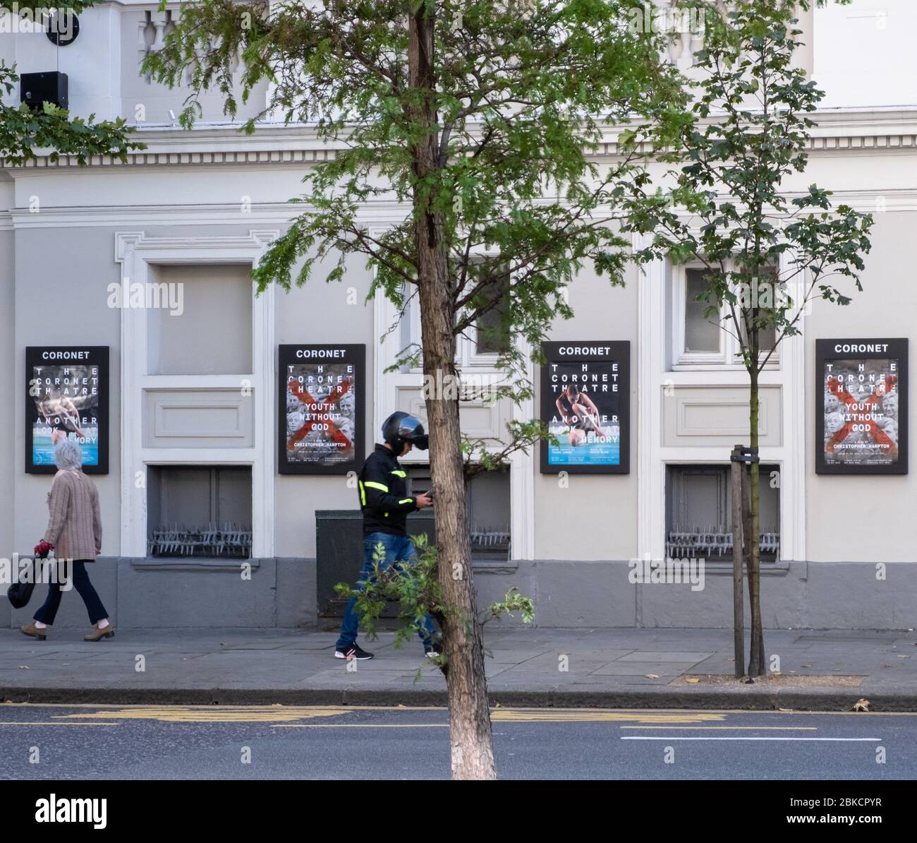 Deux personnes marchent près du théâtre Coronet, affichant des affiches pour des productions un autre regard sur mémoire et Jeunesse sans Dieu, Notting Hill, West London. Banque D'Images
