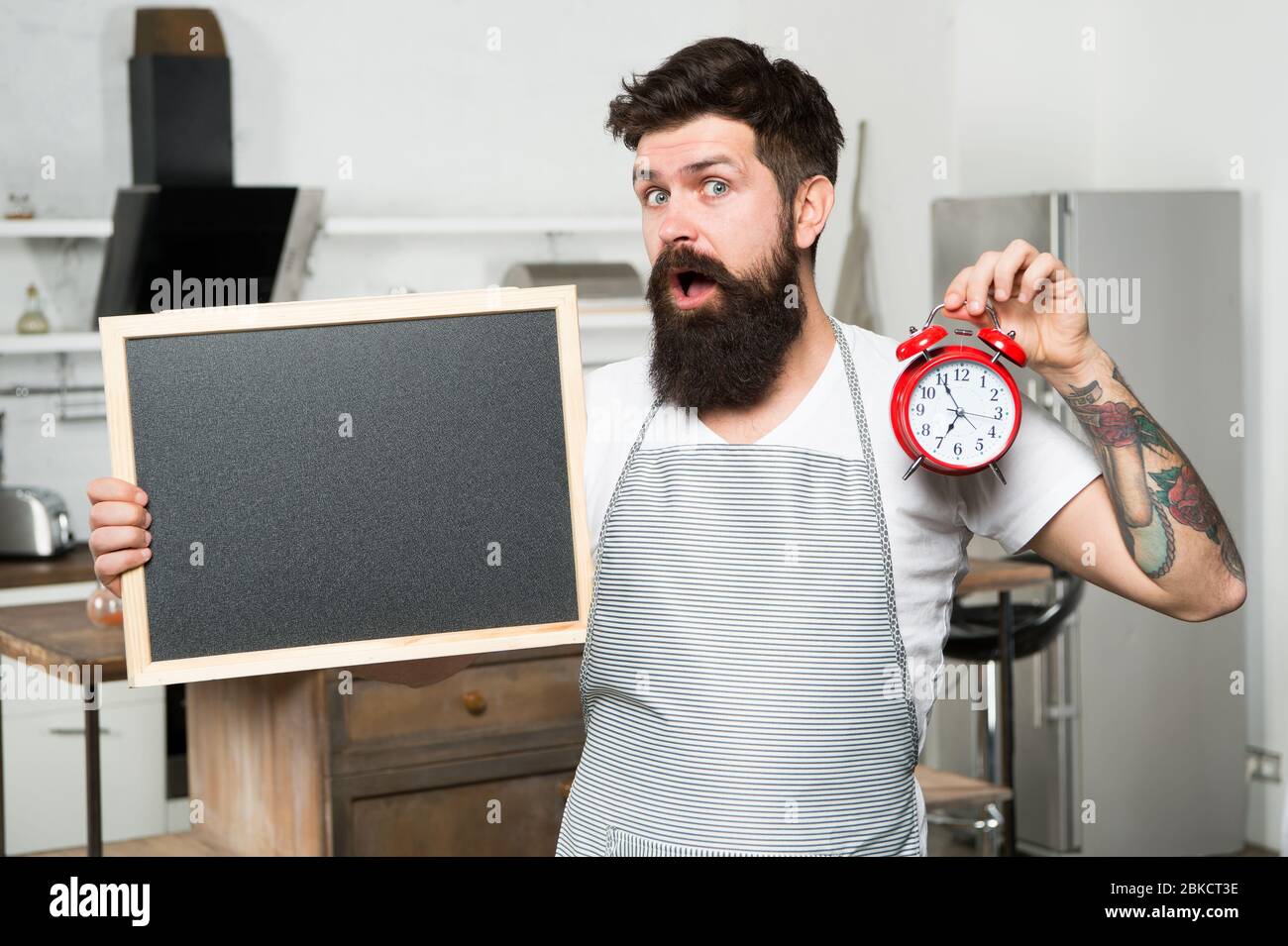 Temps de préparer des repas sains. Juste à temps. Livraison. Homme avec espace de copie de tableau noir. Cuisine de chef avec horloge. Le temps de manger. Heure du dîner. Cuisinier Hipster. Régime à jeun. Information sur le restaurant. Banque D'Images