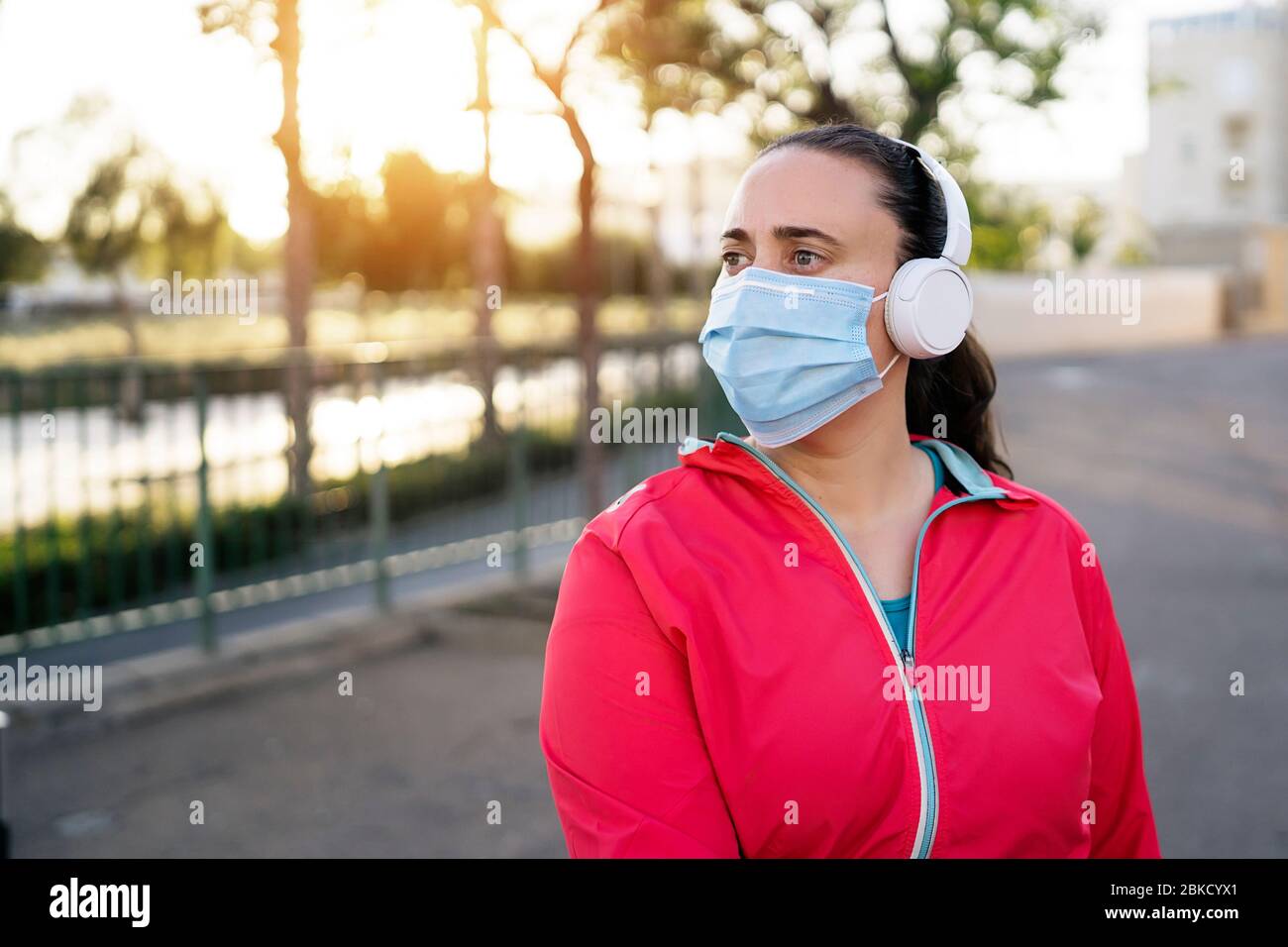 Jeune femme coureur portant un masque médical et un casque pendant le coucher du soleil. Pandémie de coronavirus Covid-19. Sport, vie active en quarantaine à Corona Outbrea Banque D'Images