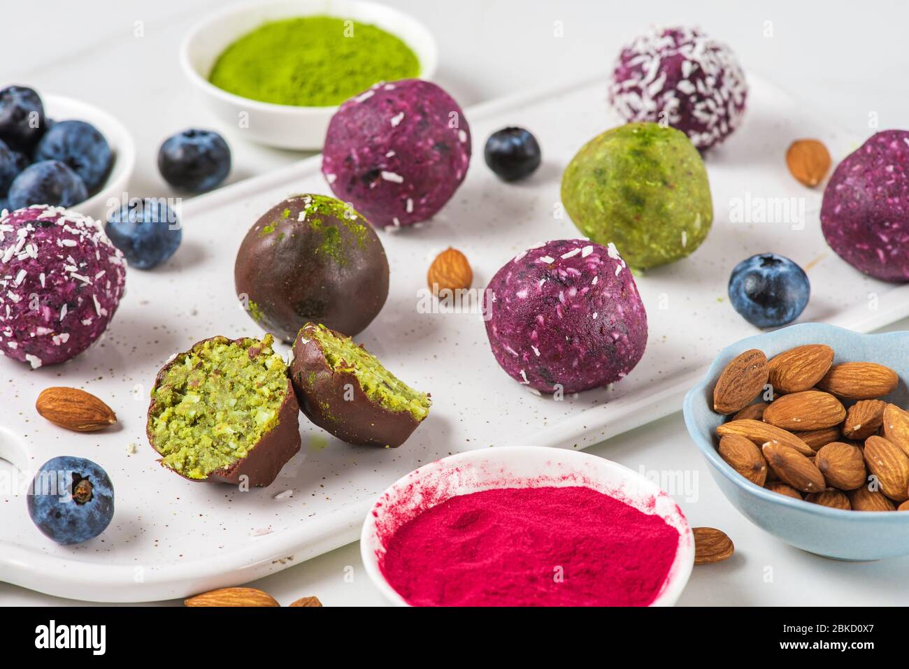 Morsures énergétiques faites d'acai, de matcha, de noix, de dattes et de baies avec des boules d'énergie dans le glaçage coloré au chocolat. Dessert végétalien sain Banque D'Images