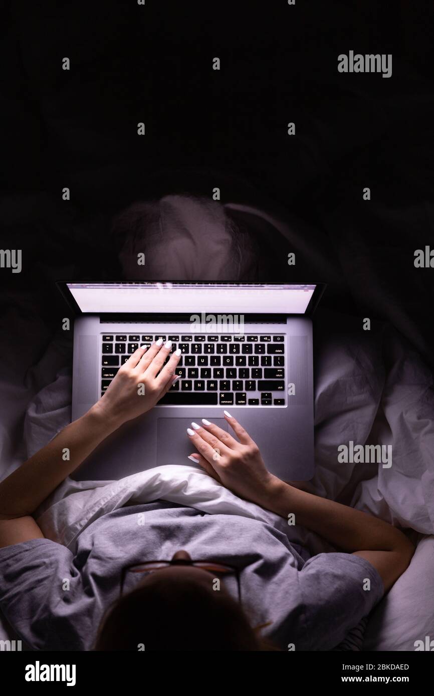 Femme dans des verres allongé dans le lit couvert par la couverture et travaillant sur ordinateur portable tard dans la nuit, ne peut pas dormir, nouvelles accro au sujet de Covid-19 ou partager social medi Banque D'Images