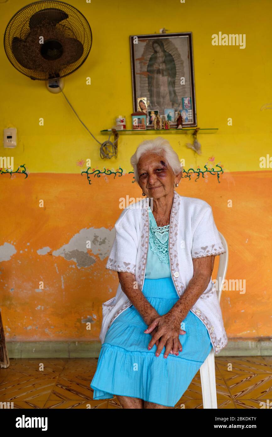 Portrait d'une vieille femme à côté d'une photo de la Vierge Marie dans une pièce avec peinture écaillée. Banque D'Images