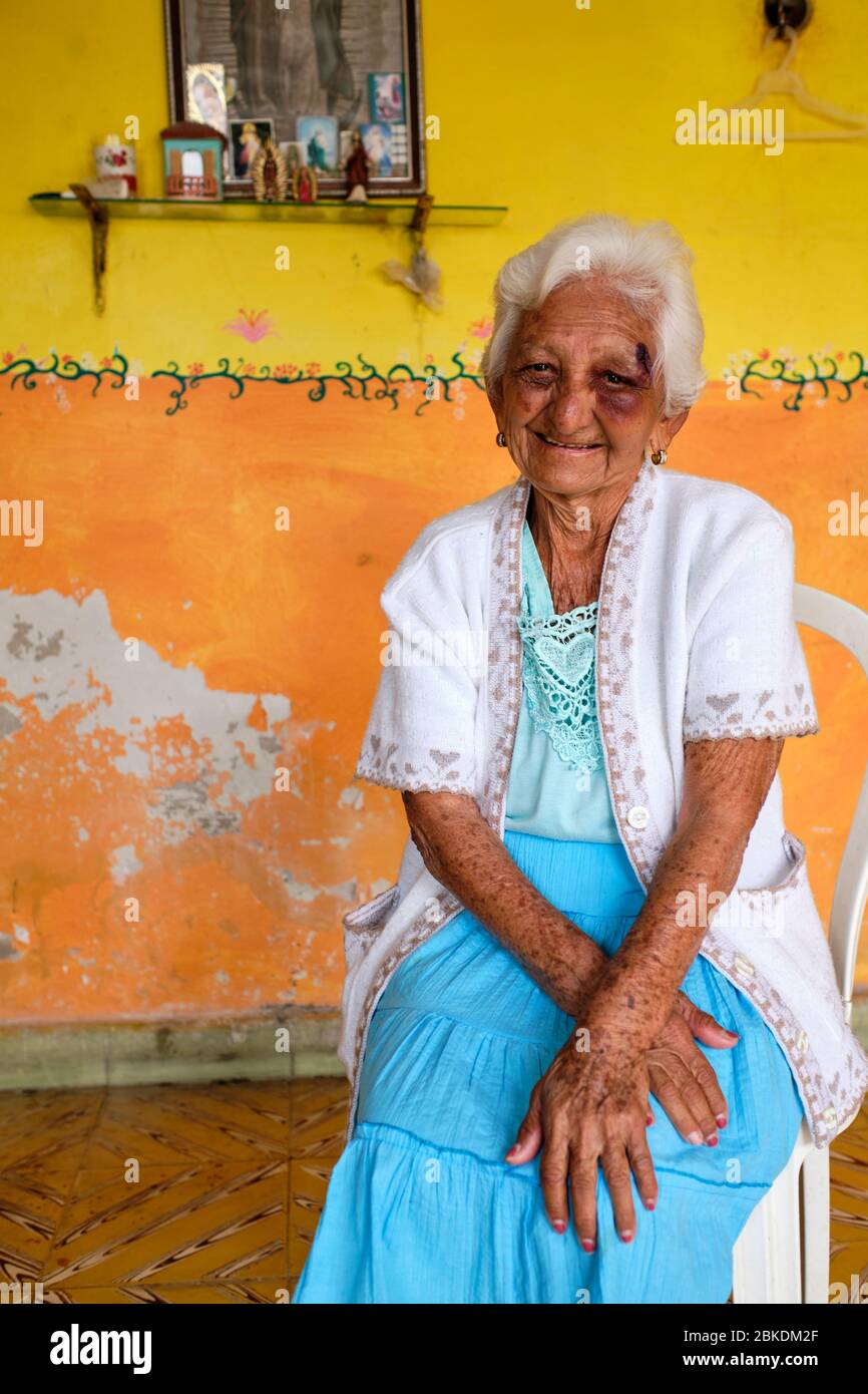 Portrait d'une vieille femme à côté d'une photo de la Vierge Marie dans une pièce avec peinture écaillée. Banque D'Images