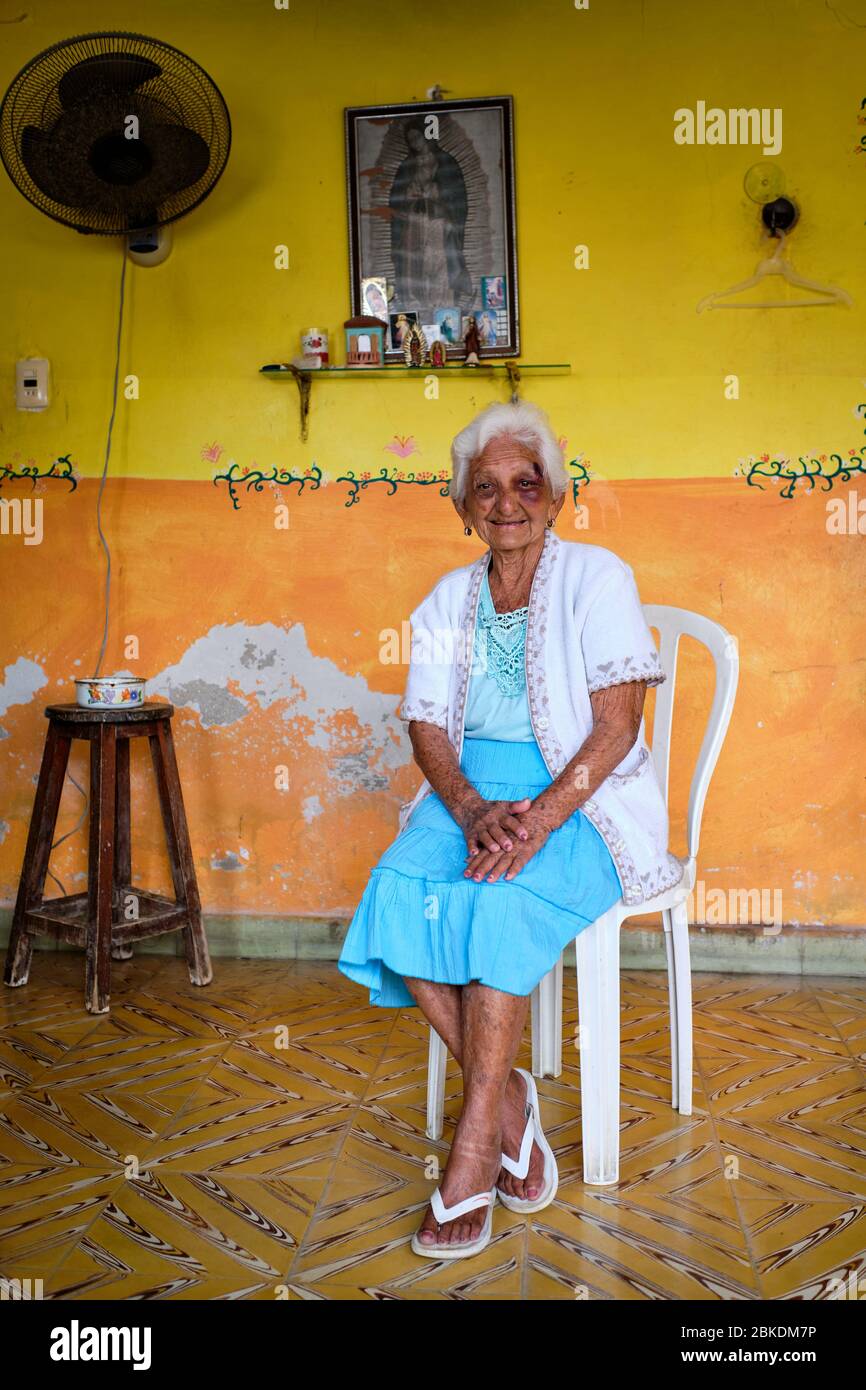 Portrait d'une vieille femme à côté d'une photo de la Vierge Marie dans une pièce avec peinture écaillée. Banque D'Images